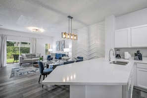 Een moderne keuken met witte kasten, een groot eiland en een eethoek met blauwe stoelen.