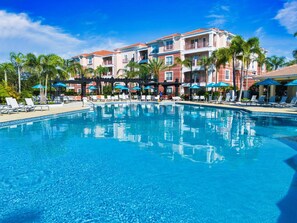 A clear blue pool with lounge chairs and umbrellas, surrounded by palm trees and a building with balconies. - Th14 - 3BR House With Pool Access Near Disney (Orlando)