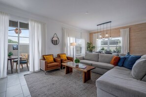Een moderne woonkamer met een bank, twee fauteuils, een salontafel en een eethoek met een tafel en stoelen.