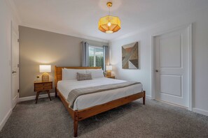 Een slaapkamer met een houten bed, twee nachtkastjes met lampen, een raam met gordijnen en een deur.