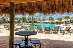 A poolside area with lounge chairs, a round table, and a thatched roof structure. - Sl4359 - 5BR House With Pool Near Disney (Kissimmee)