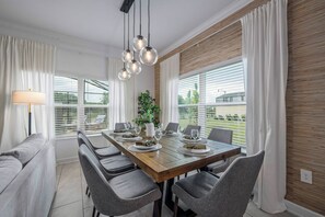 A dining area with a wooden table set for six, surrounded by grey chairs, with a potted plant and a lamp on the table. - Sl4359 - 5BR House With Pool Near Disney (Kissimmee)