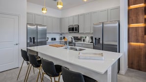 Een moderne keuken met witte kasten, roestvrijstalen apparatuur, een centraal eiland met barkrukken en hanglampen.