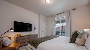 A bedroom with a large bed, a TV mounted on the wall, a dresser, and a window with a view of a balcony. - Wi3277 - 5BR House Near Disney With Private Pool (Davenport)