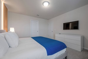 A bedroom with a bed, white walls, a ceiling light, a TV mounted on the wall, and a white dresser. - Wi3277 - 5BR House Near Disney With Private Pool (Davenport)