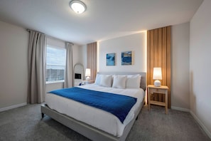 Una habitación de hotel ordenada con una cama grande, dos mesitas de noche con lámparas, una ventana con cortinas y dos cuadros colgados en la pared.