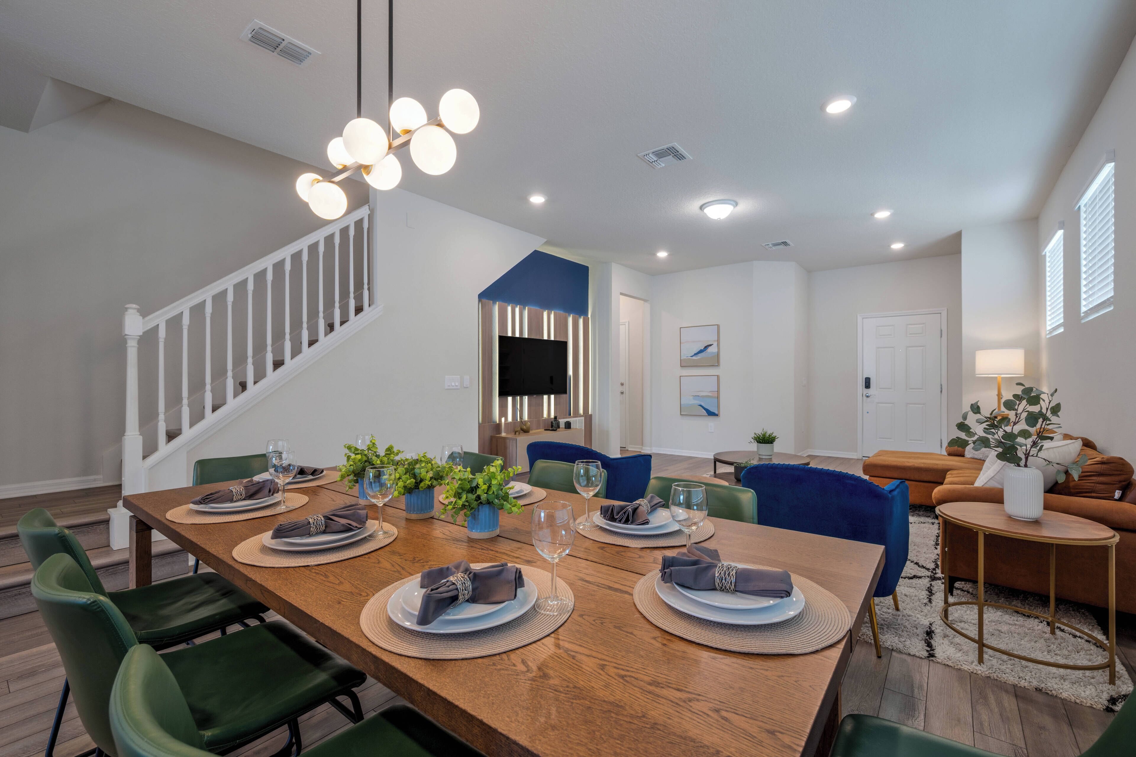 Un espace repas avec une table en bois dressée pour six personnes, entourée de chaises vertes, et un escalier menant à un niveau supérieur.