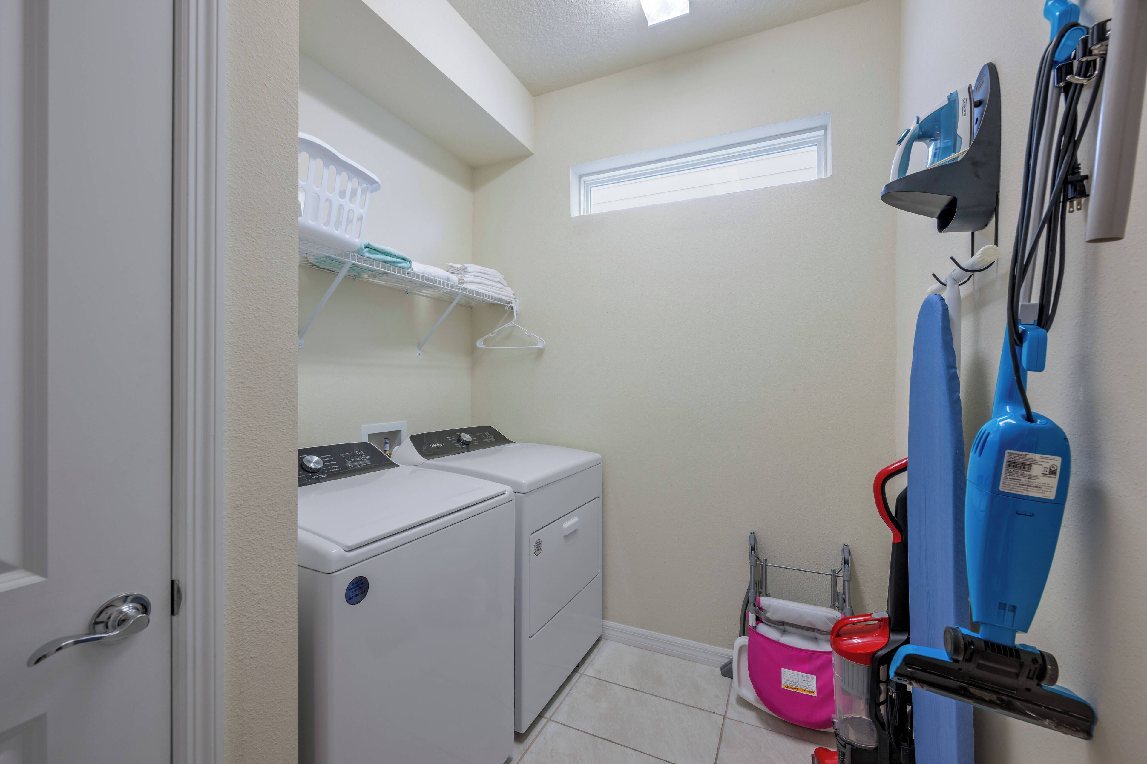 A laundry room with two stacked washers and dryers, a drying rack, and a blue vacuum cleaner.