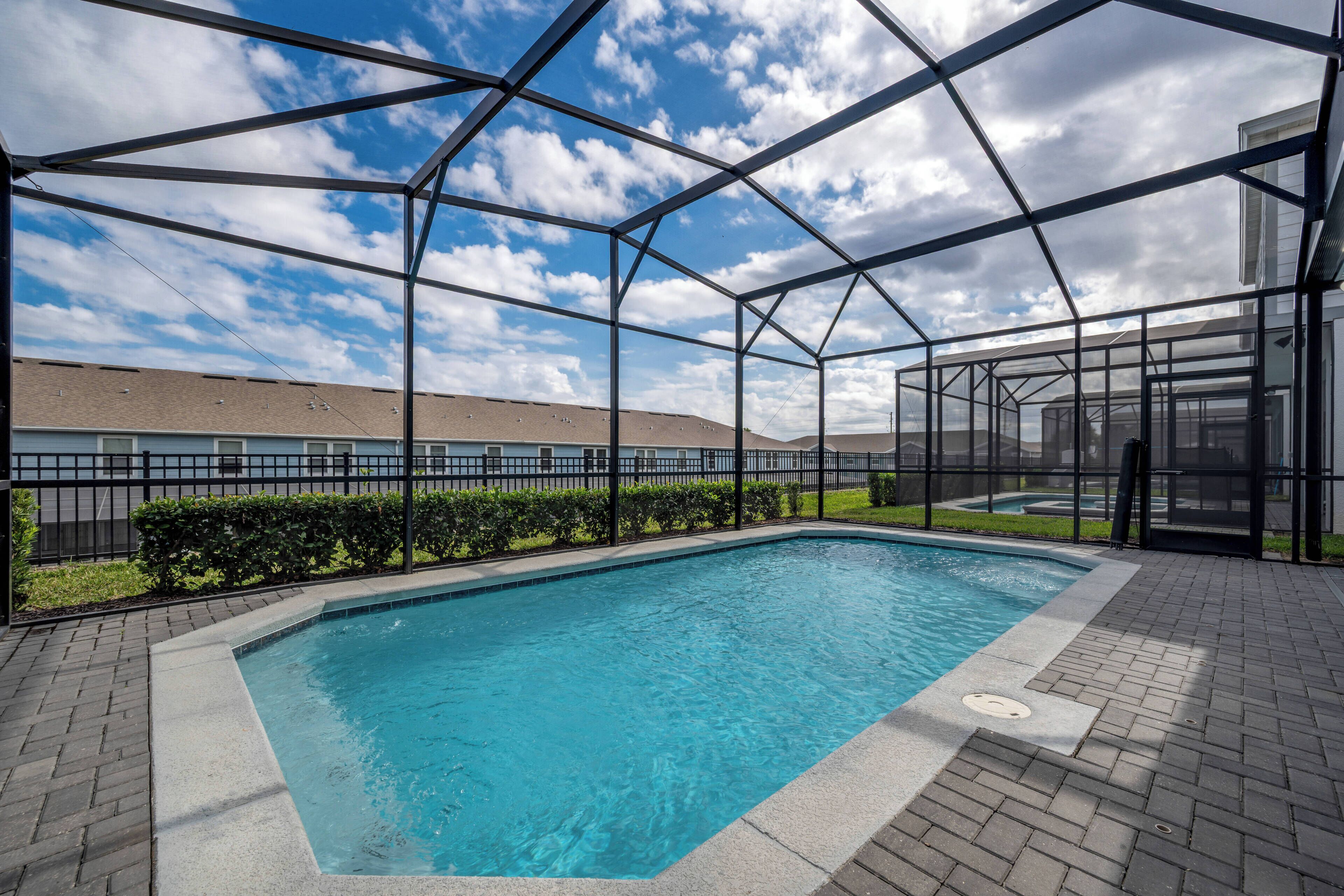 A swimming pool with a clear blue water, surrounded by a metal frame structure, and a paved walkway.