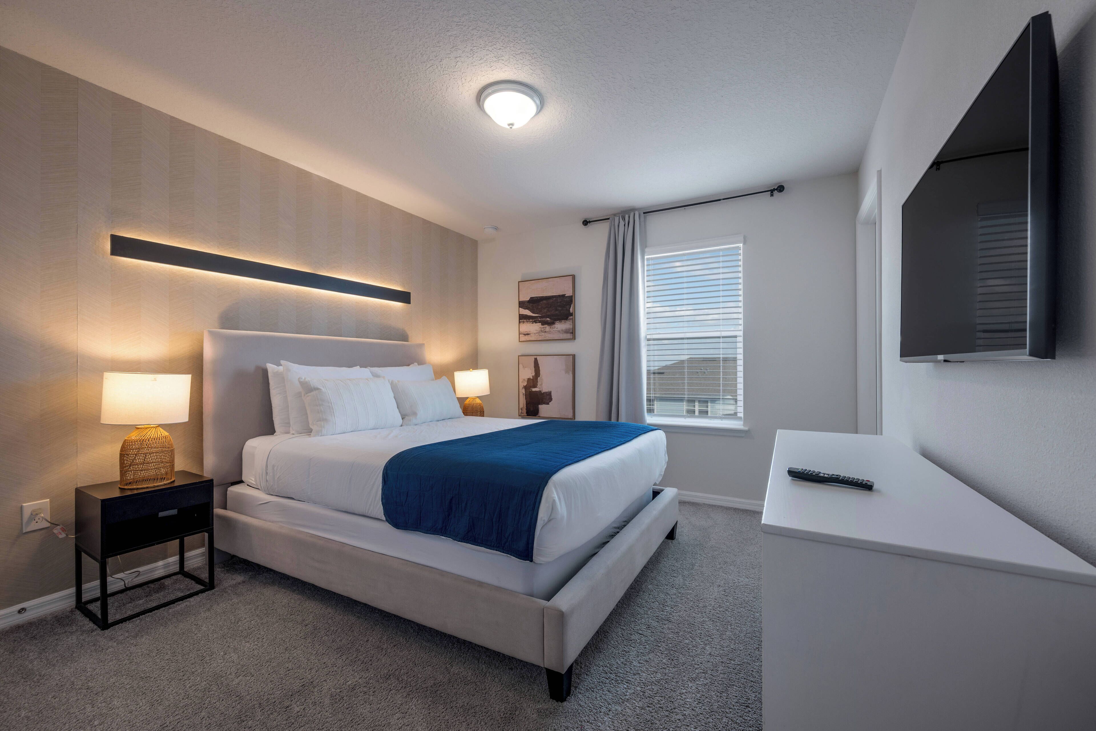 A modern hotel room with a large bed, bedside lamps, a flat-screen TV, and a window with blinds.