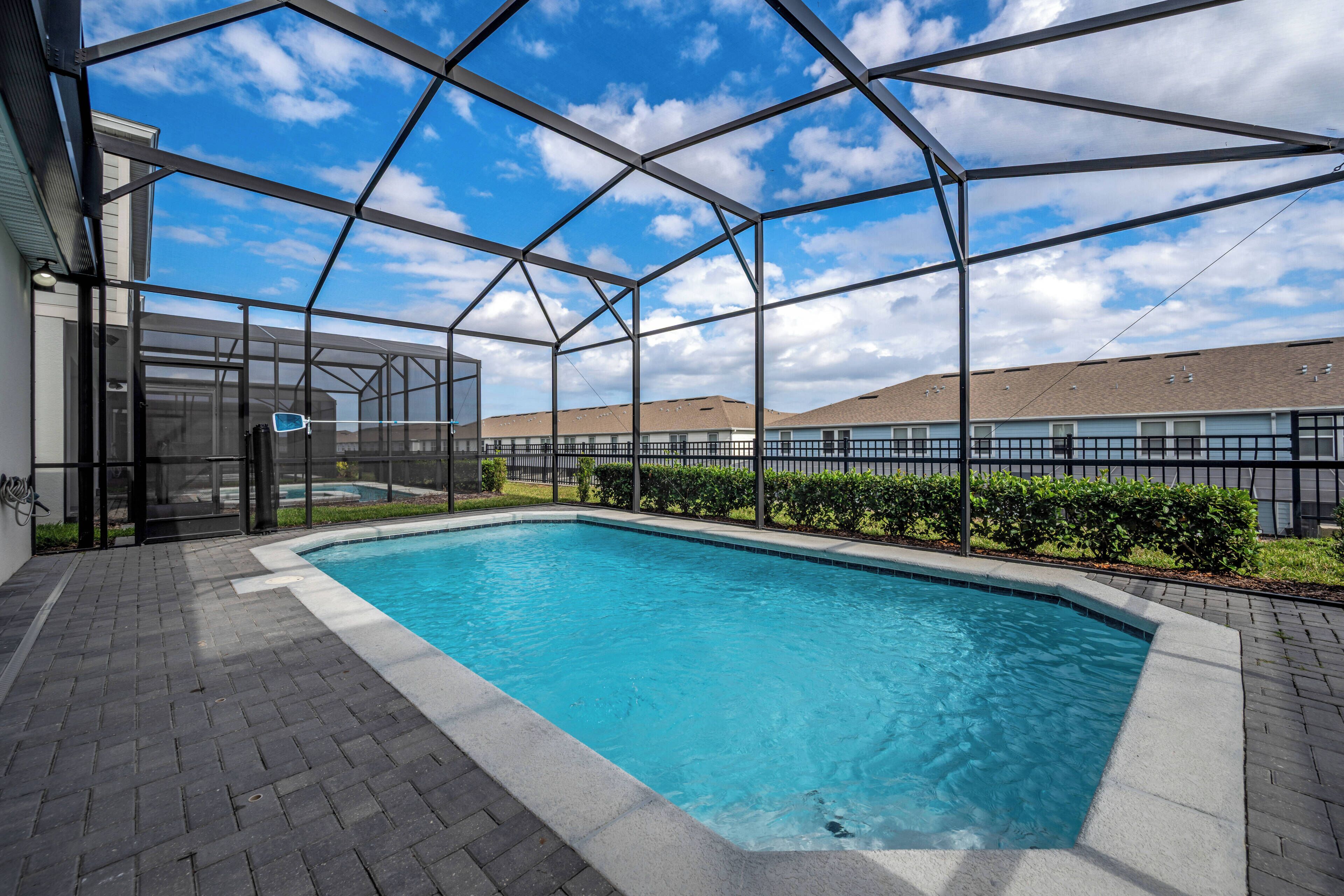A swimming pool with a glass enclosure, surrounded by a brick patio and a hedge.