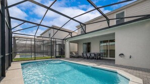 A swimming pool with a covered patio area, a table with chairs, and a view of a house in the background. - Wi3277 - 5BR House Near Disney With Private Pool (Davenport)
