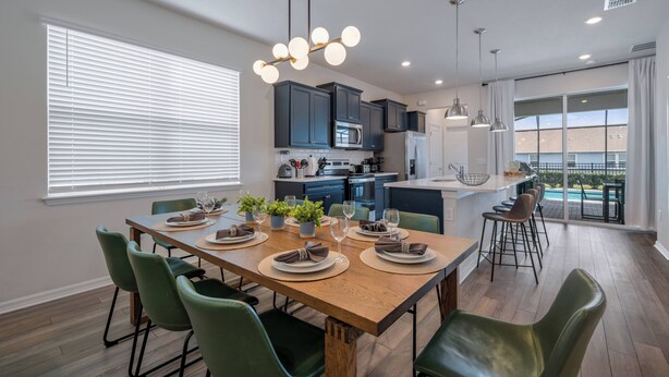 A modern kitchen with dark cabinets, a wooden dining table set with plates, glasses, and a plant. - Wi3277 - 5BR House Near Disney With Private Pool (Davenport)