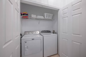 Un cuarto de lavandería con lavadora y secadora de carga frontal, un estante con toallas dobladas y una cesta.