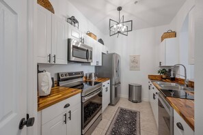 A compact kitchen with white cabinets, stainless steel appliances, a wooden countertop, and a black rug. - Wp304 - 2BR Fully Renovated Condo - Windsor Palms (Kissimmee)