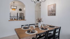 A dining area with a wooden table set for four, surrounded by black chairs. There is a chandelier above the table, a vase with dried flowers on the table, and a framed picture on the wall. - Wp304 - 2BR Fully Renovated Condo - Windsor Palms (Kissimmee)