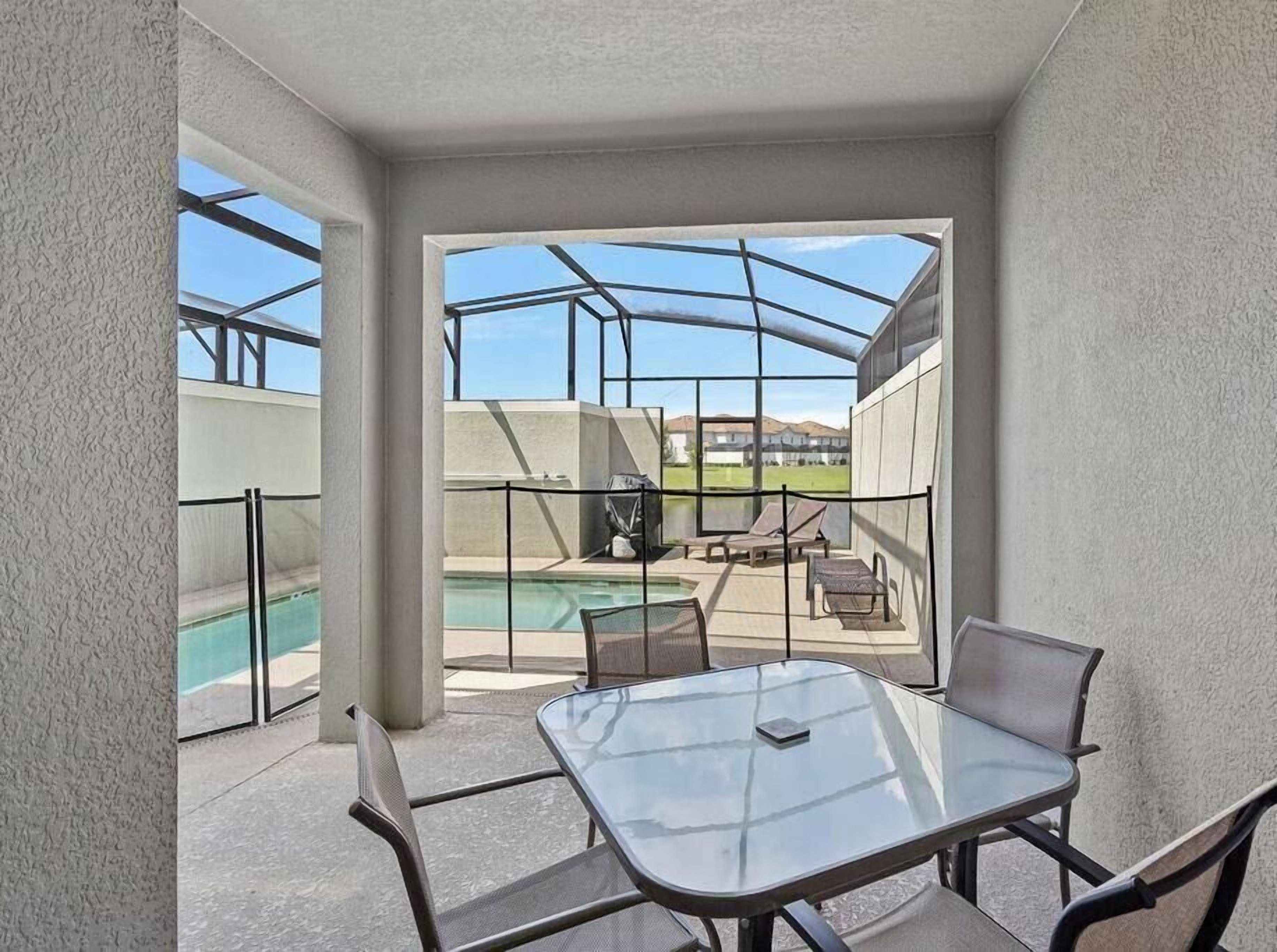 Un espacio al aire libre cubierto con una mesa y sillas de vidrio, una piscina y sillones de descanso.
