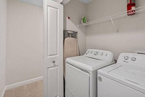 A laundry room with two white front-loading washers and dryers, a white door, a beige towel on a rack, and a red fire extinguisher on a white shelf. - Sl3095 - 4BR House With Pool Near Disney Parks (Kissimmee)