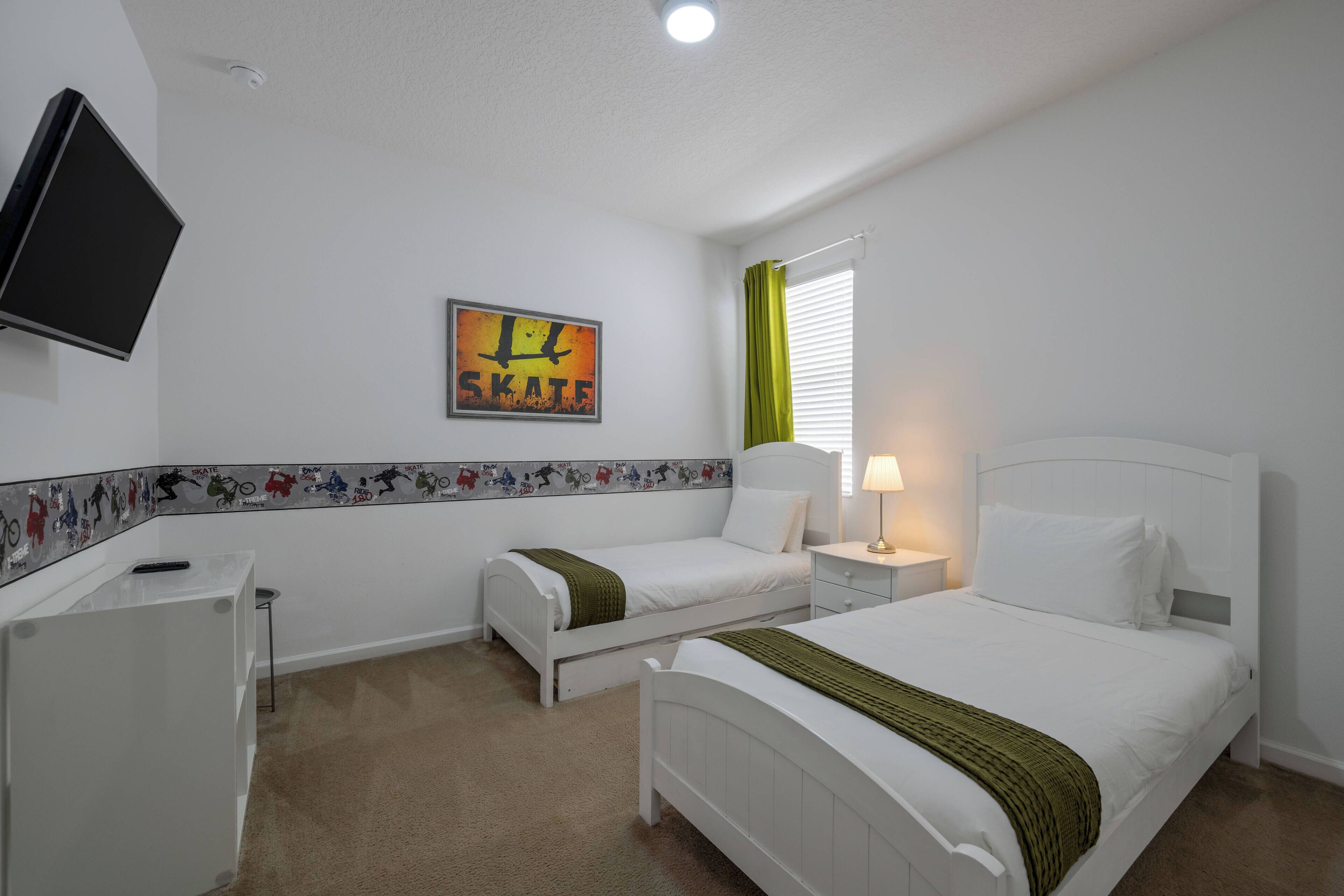 Une chambre avec deux lits, un téléviseur fixé au mur, un tableau et une fenêtre avec des rideaux.