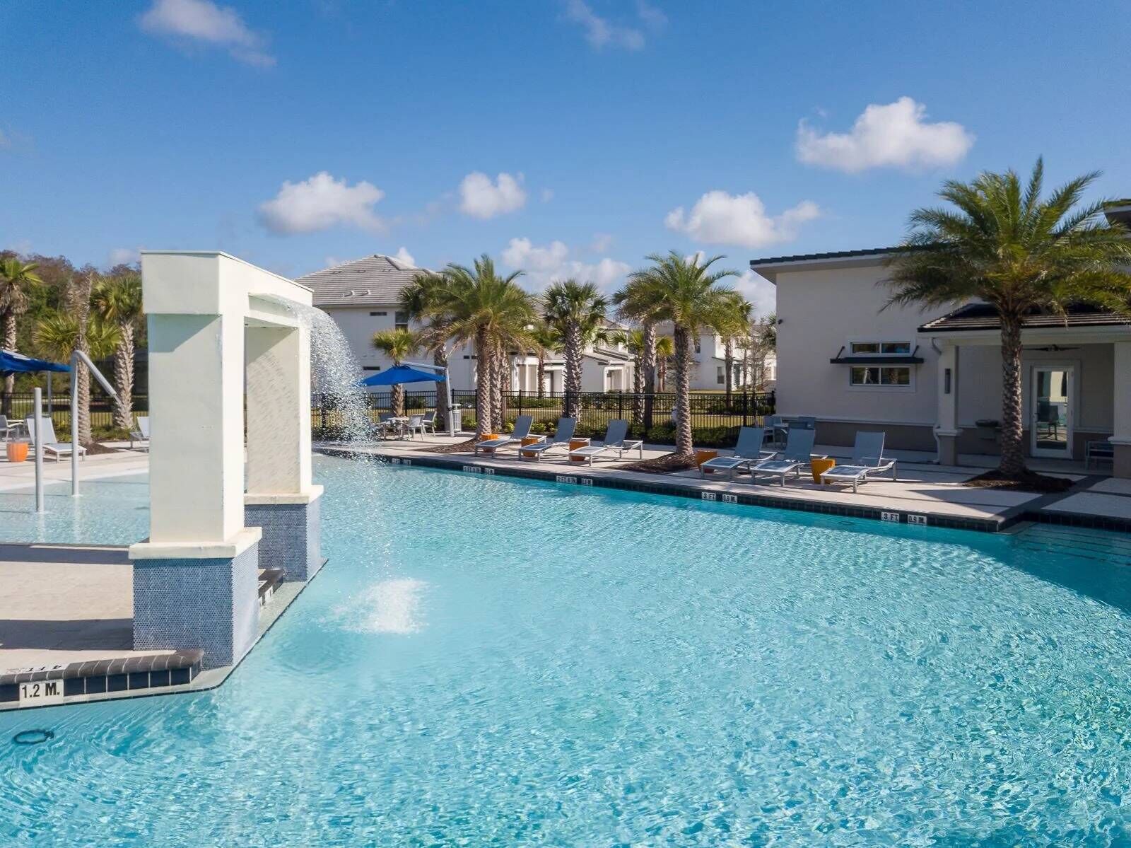 A clear blue pool with lounge chairs and palm trees, surrounded by buildings.