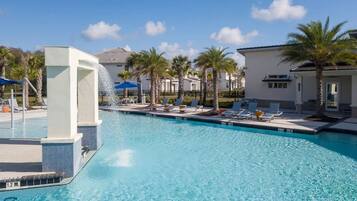 A clear blue pool with lounge chairs and palm trees, surrounded by buildings.