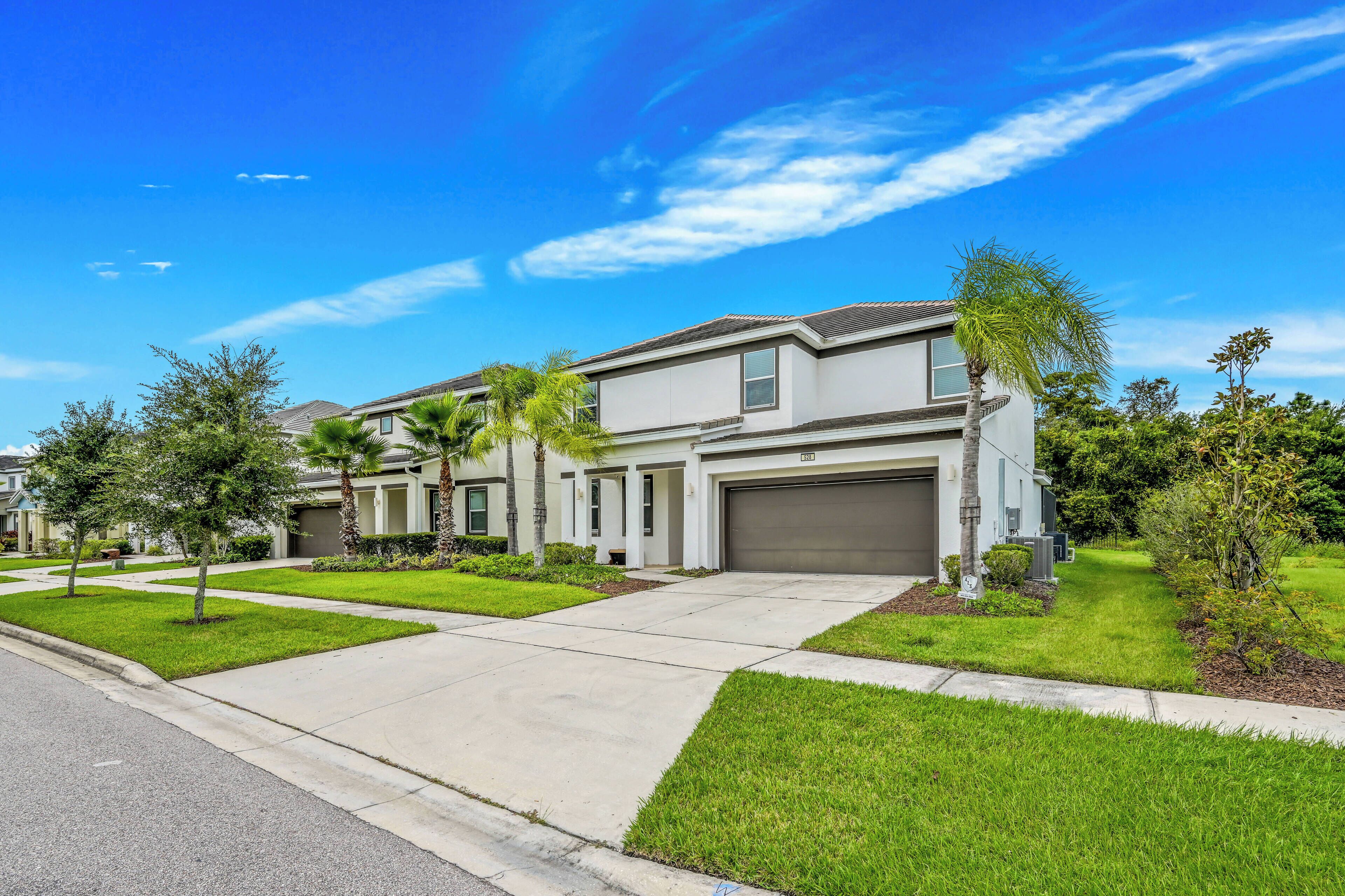 A modern two-story house with a garage, surrounded by well-maintained lawns and palm trees.