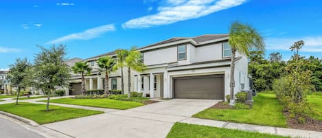 A modern two-story house with a garage, surrounded by well-maintained lawns and palm trees.