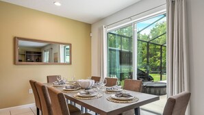 Un comedor con una mesa grande dispuesta para seis personas, rodeada de sillas, con un ventanal y una puerta corrediza de cristal que da a un espacio exterior.