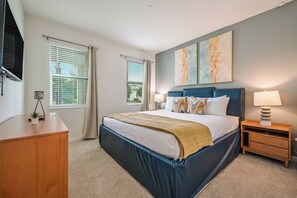 A bedroom with a large bed, two bedside lamps, a wooden nightstand, and a wall-mounted TV. - Bv528 - 6BR House With Pool Near Disney (Kissimmee)