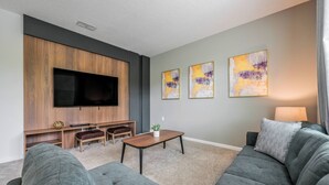 Una sala de estar moderna con un televisor de pantalla plana grande, sofás grises, un mueble de entretenimiento de madera y arte abstracto en la pared.