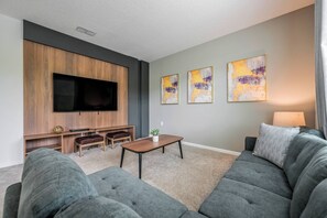 Ein modernes Wohnzimmer mit einem großen Flachbildfernseher, grauen Sofas, einer Holztrennwandschränken und abstrakten Wandbildern.