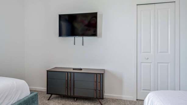Un dormitorio con televisión montada en la pared, un aparador y una puerta blanca.