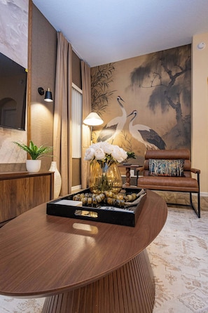 Un salon moderne avec une table basse en bois, un canapé agrémenté de coussins à motifs, un téléviseur fixé au mur et un tableau décoratif représentant des oiseaux.