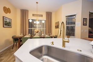 A modern kitchen with a large island, stainless steel sink, and gold faucets. - Tu220 - 5BR House With Pool Near Disney Area (Davenport)