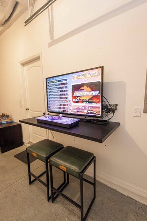 A gaming setup with a monitor displaying a fighting game, a keyboard, and two green cushioned stools. - Tu220 - 5BR House With Pool Near Disney Area (Davenport)