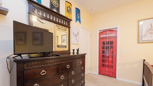 A room with a wooden dresser, a flat-screen TV, a red telephone booth, and a door with a white frame. - Tu220 - 5BR House With Pool Near Disney Area (Davenport)