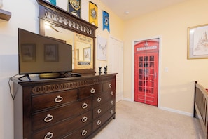 A room with a wooden dresser, a flat-screen TV, a red telephone booth, and a door with a white frame. - Tu220 - 5BR House With Pool Near Disney Area (Davenport)