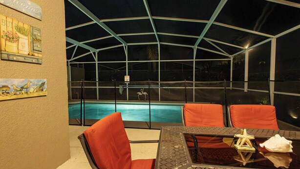 A covered outdoor area with a pool, orange chairs, and a table with a star decoration. - Tu220 - 5BR House With Pool Near Disney Area (Davenport)