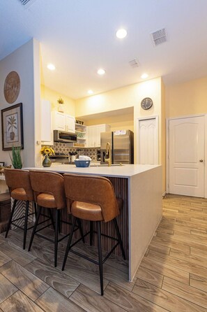 A modern kitchen with a central island, bar stools, and stainless steel appliances. - Tu220 - 5BR House With Pool Near Disney Area (Davenport)