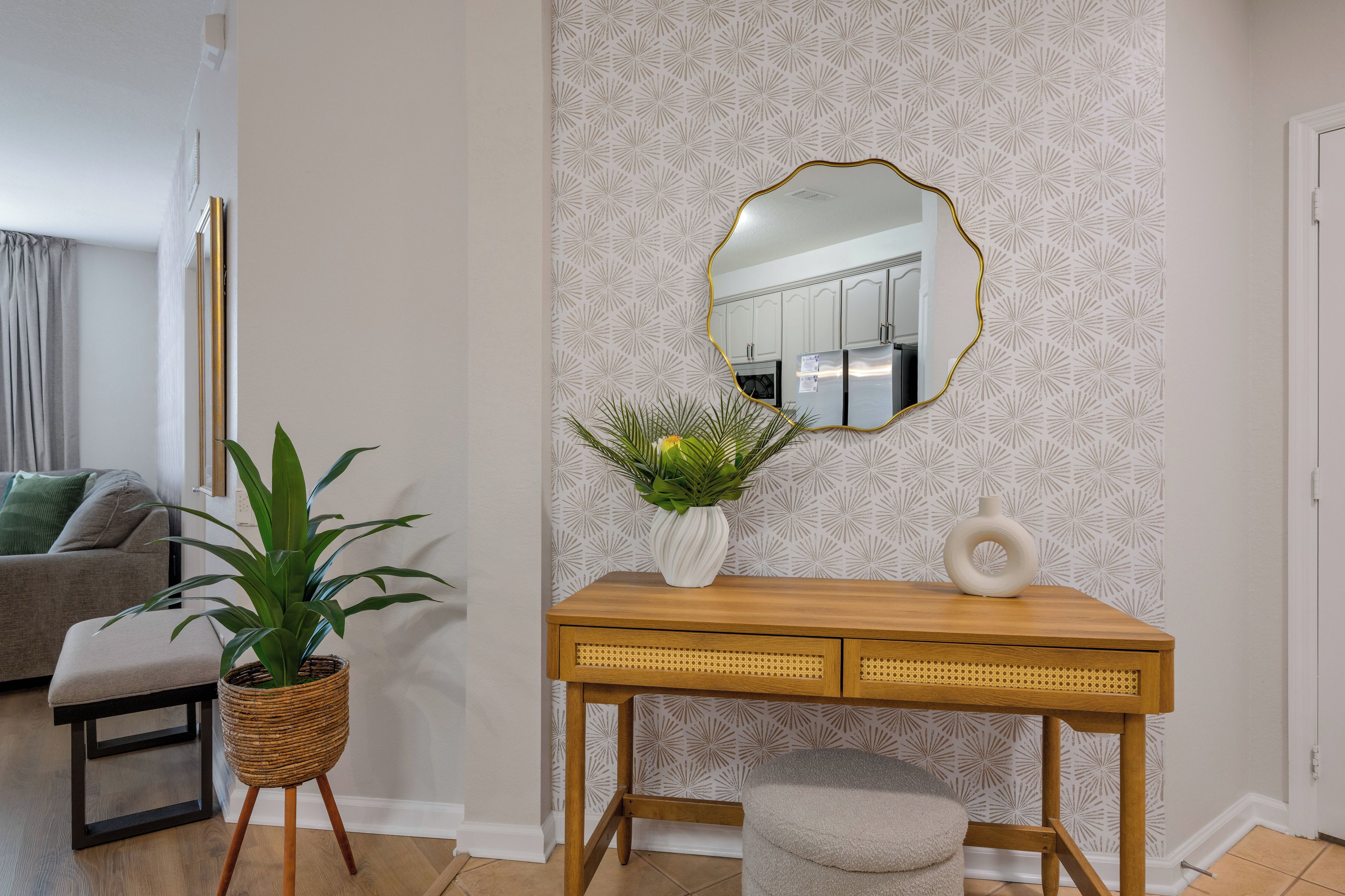 A living room with a wooden console table, a potted plant, a mirror, and a patterned wallpaper.