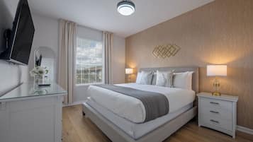 A modern hotel room with a large bed, bedside lamps, a flat-screen TV, and a glass desk with a vase of flowers.