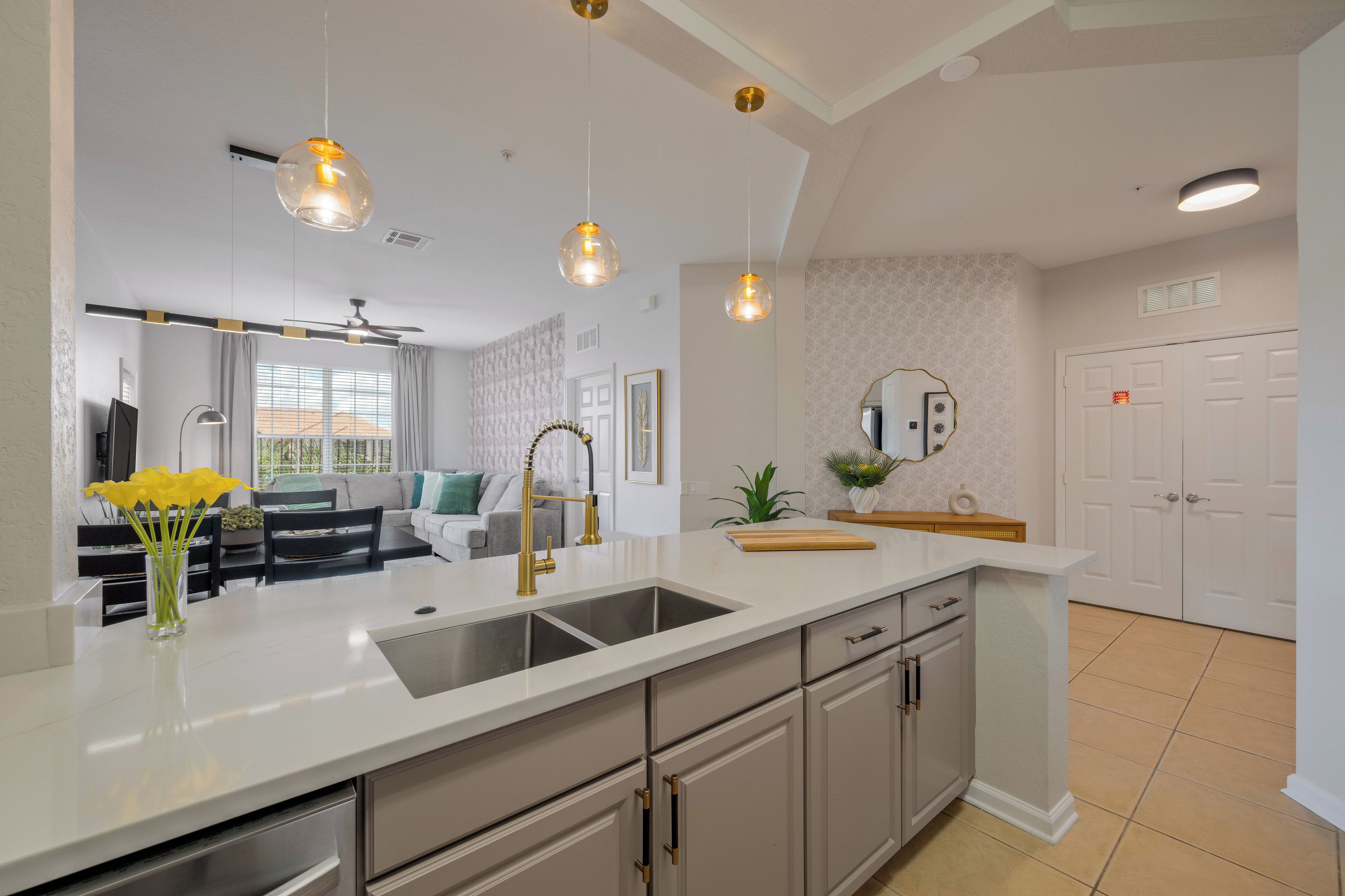 A modern kitchen with a white countertop, stainless steel sink, and a dining area with a sofa and table.