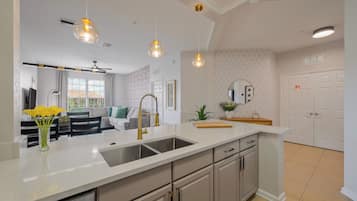 A modern kitchen with a white countertop, stainless steel sink, and a dining area with a sofa and table.