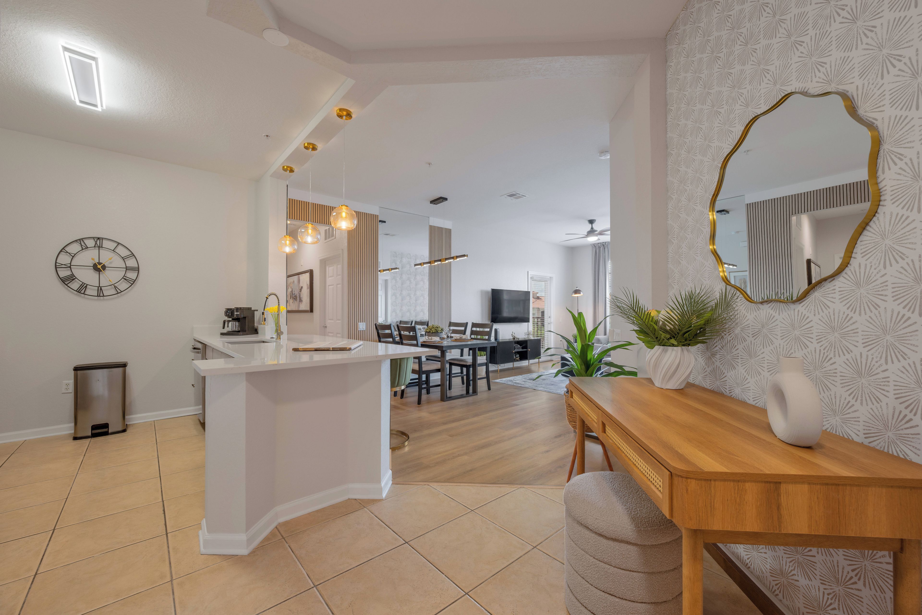 Una cocina moderna con una isla central, un comedor con mesa de madera y una sala de estar con televisor y asientos.