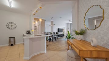 Una cocina moderna con una isla central, un comedor con mesa de madera y una sala de estar con televisor y asientos.