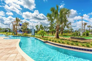 Una piscina con un borde de baldosas, palmeras y un cielo azul despejado.