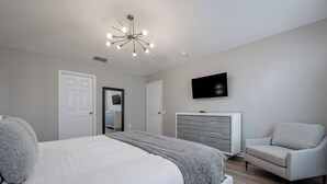 Un dormitorio con una cama, televisión, sillón y cómoda.