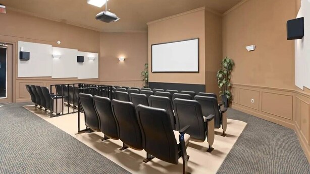 Un salón de conferencias con filas de sillas negras, una pizarra y una pantalla para proyector.