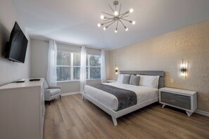 A modern bedroom with a bed, bedside tables, a TV, and a window with blinds. - Wh7712 - 6BR House w/ Resort Access Near Disney (Kissimmee)