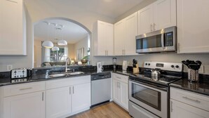 Una cocina moderna con armarios blancos, electrodomésticos de acero inoxidable y encimera negra.